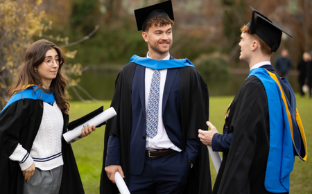 UCD graduates stand together outdoors after their conferring ceremony, wearing academic gowns.